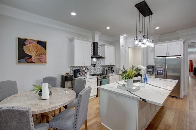 kitchen featuring white cabinetry, hanging light fixtures, stainless steel appliances, and wall chimney range hood