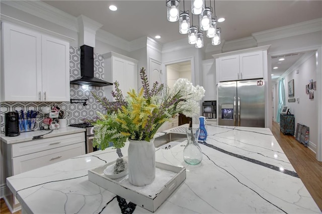 kitchen featuring wall chimney exhaust hood, white cabinetry, stainless steel appliances, and decorative light fixtures