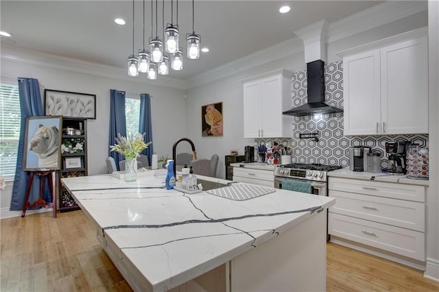 kitchen with white cabinets, wall chimney range hood, a kitchen island with sink, and stainless steel stove