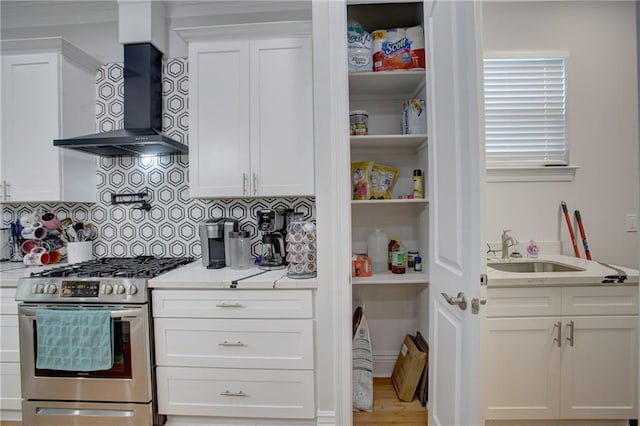 kitchen featuring white cabinets, wall chimney exhaust hood, sink, and stainless steel gas range