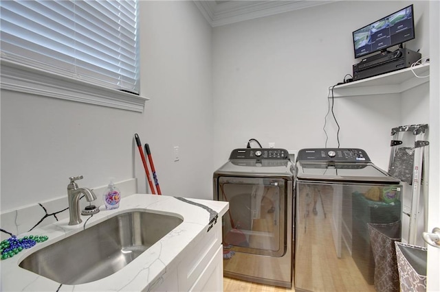 laundry area featuring washing machine and clothes dryer, light hardwood / wood-style floors, ornamental molding, and sink