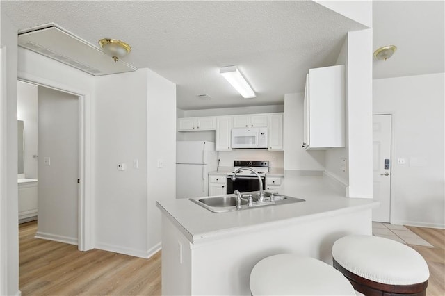 kitchen with white appliances, white cabinets, light wood-type flooring, a textured ceiling, and kitchen peninsula