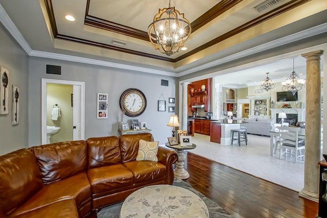 living room with ornate columns, a raised ceiling, crown molding, a chandelier, and wood-type flooring