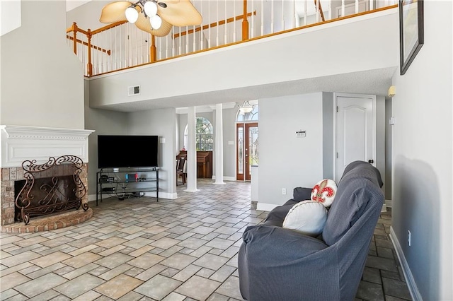 living room with a towering ceiling, decorative columns, a brick fireplace, and ceiling fan