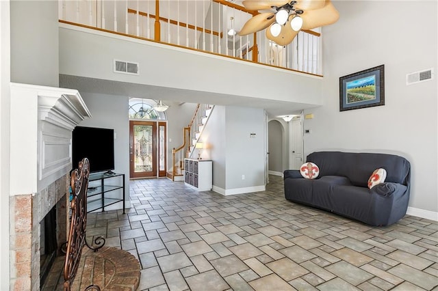 living room with ceiling fan, a towering ceiling, and a tiled fireplace