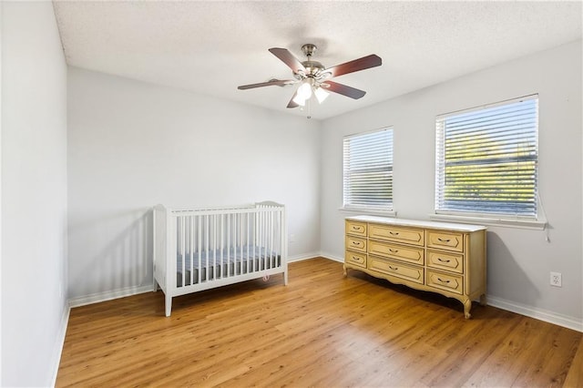 bedroom featuring ceiling fan, a crib, light wood-type flooring, and a textured ceiling