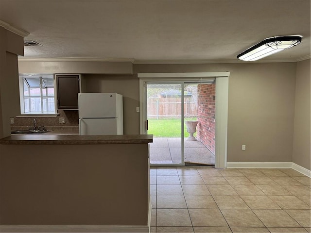 kitchen with sink, white refrigerator, decorative backsplash, light tile patterned floors, and ornamental molding