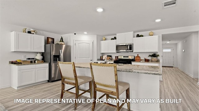 kitchen with a breakfast bar, stainless steel appliances, a center island with sink, light hardwood / wood-style floors, and white cabinetry