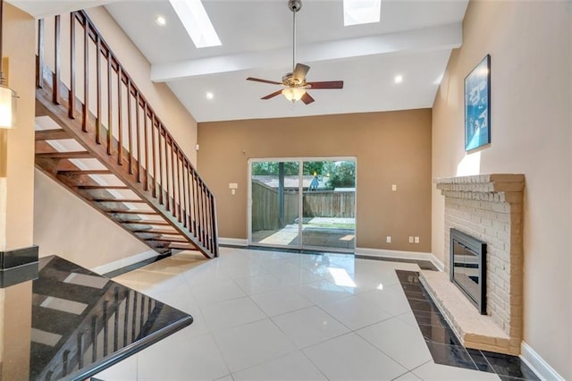 tiled living room featuring high vaulted ceiling, a fireplace, beamed ceiling, a skylight, and ceiling fan