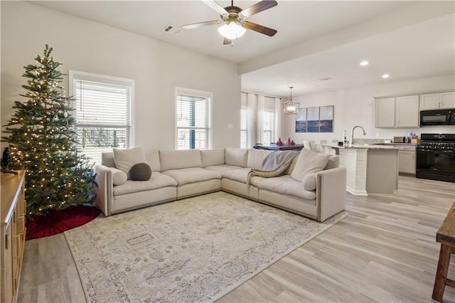 living room featuring ceiling fan with notable chandelier and light wood-type flooring