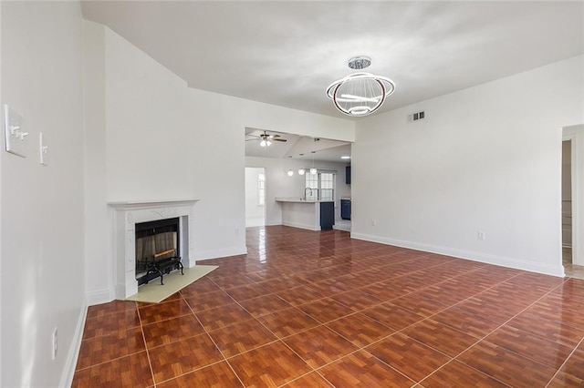 unfurnished living room featuring ceiling fan with notable chandelier, dark tile patterned floors, and a premium fireplace