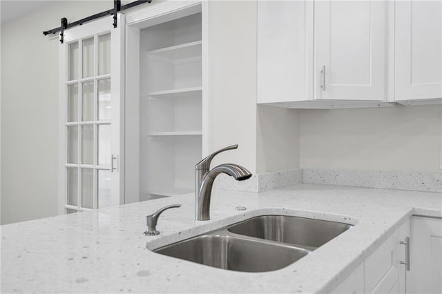 details featuring a barn door, white cabinetry, light stone counters, and sink