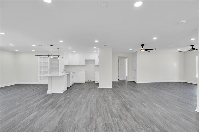 unfurnished living room with light wood-type flooring, ceiling fan, a barn door, and sink