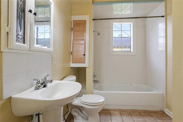 full bathroom with tasteful backsplash, tile patterned floors, tiled shower / bath combo, sink, and toilet