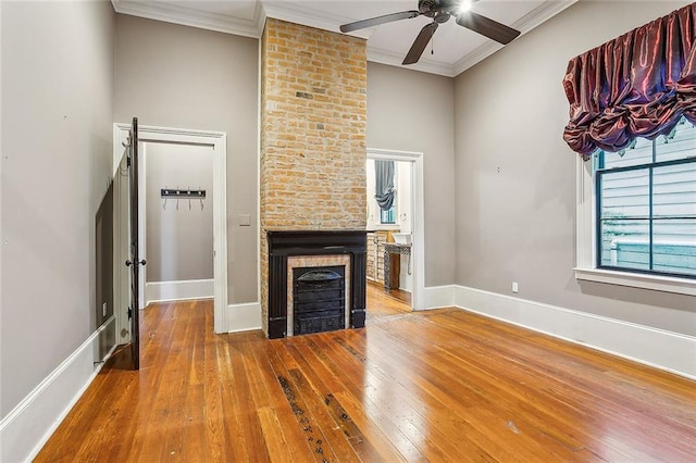 unfurnished living room with a brick fireplace, wood-type flooring, ornamental molding, and ceiling fan