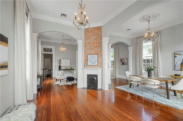 interior space featuring hardwood / wood-style flooring, a brick fireplace, decorative columns, and ornamental molding