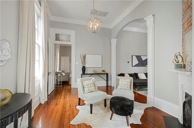 living area featuring decorative columns, an inviting chandelier, hardwood / wood-style flooring, and crown molding