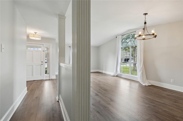 unfurnished dining area featuring ornate columns, dark hardwood / wood-style flooring, vaulted ceiling, and an inviting chandelier