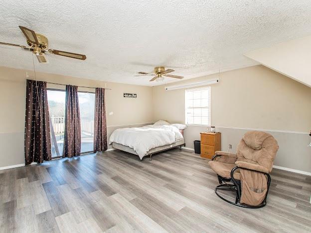 bedroom featuring access to exterior, a textured ceiling, ceiling fan, wood-type flooring, and lofted ceiling