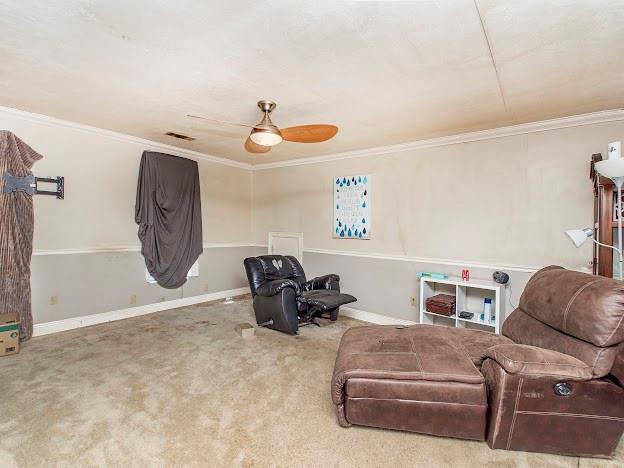 sitting room with carpet, ceiling fan, and ornamental molding