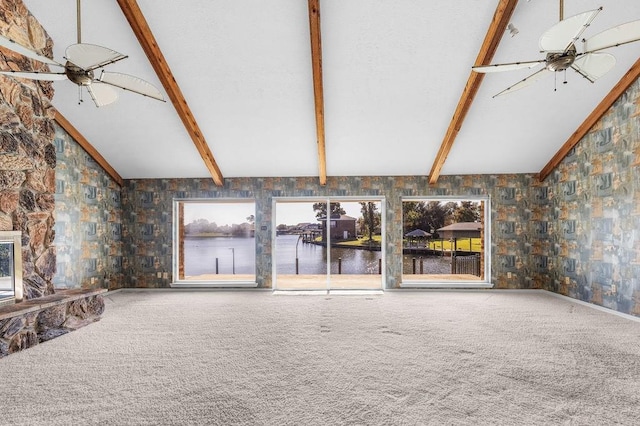 unfurnished living room with carpet, a water view, ceiling fan, and beamed ceiling