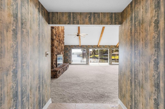 unfurnished living room with beam ceiling, ceiling fan, a fireplace, and light colored carpet