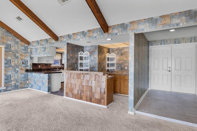 kitchen with white cabinets, vaulted ceiling with beams, carpet floors, and kitchen peninsula