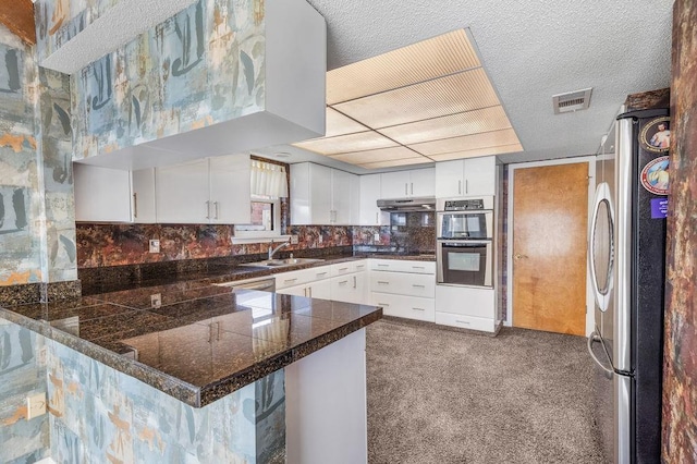 kitchen with kitchen peninsula, appliances with stainless steel finishes, dark carpet, sink, and white cabinetry