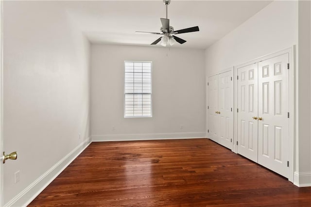 unfurnished bedroom featuring dark hardwood / wood-style flooring, ceiling fan, and multiple closets