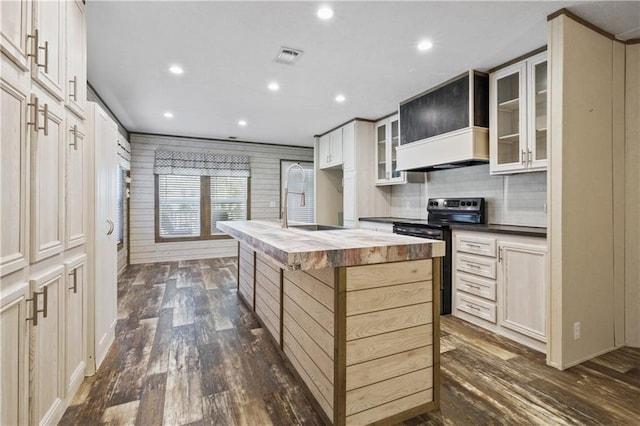 kitchen featuring dark wood-type flooring, wooden counters, an island with sink, black range with electric cooktop, and tasteful backsplash