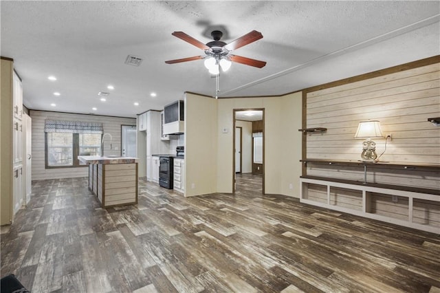 kitchen with dark hardwood / wood-style flooring, a textured ceiling, wooden walls, black electric range oven, and a breakfast bar area