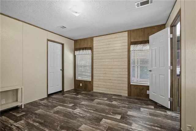 spare room featuring a textured ceiling, wooden walls, and dark wood-type flooring