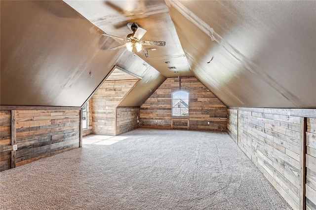 bonus room with wooden walls, ceiling fan, vaulted ceiling, and light colored carpet