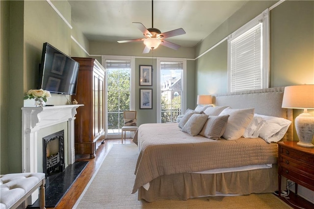 bedroom with multiple windows, ceiling fan, a premium fireplace, and wood-type flooring