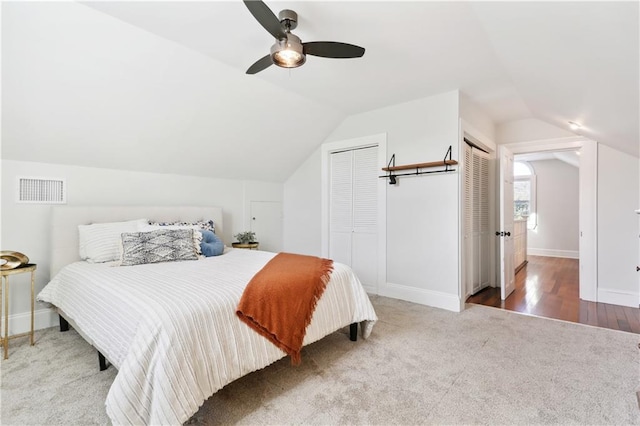 bedroom featuring multiple closets, ceiling fan, lofted ceiling, and hardwood / wood-style flooring