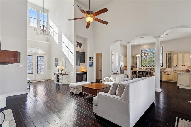 living room with decorative columns, dark wood-type flooring, ceiling fan with notable chandelier, and french doors