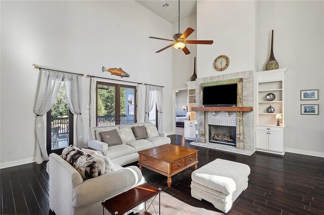 living room featuring decorative columns, a brick fireplace, dark wood-type flooring, and ceiling fan