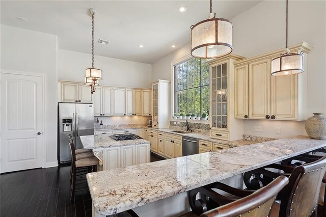 kitchen with sink, a breakfast bar area, appliances with stainless steel finishes, light stone countertops, and decorative light fixtures