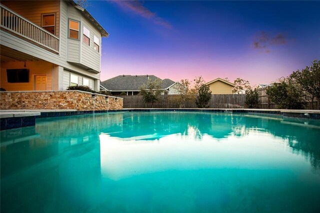 pool at dusk featuring a patio and an in ground hot tub