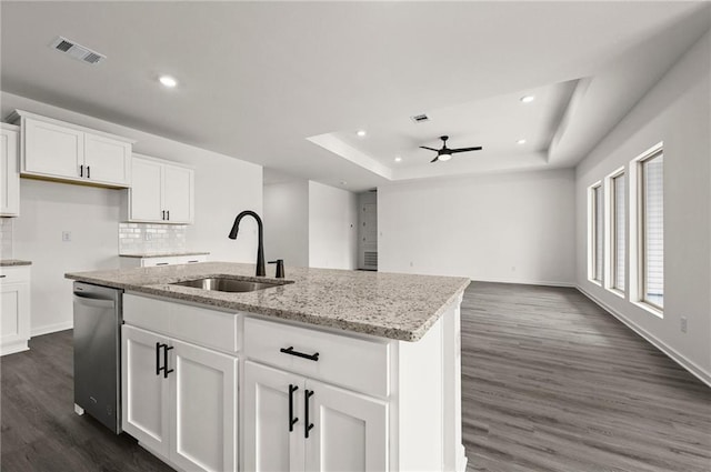 kitchen featuring sink, stainless steel dishwasher, an island with sink, a tray ceiling, and dark hardwood / wood-style flooring