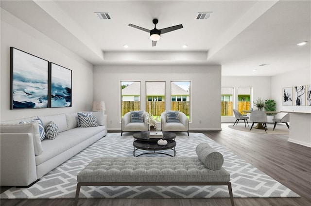 living room with hardwood / wood-style flooring, ceiling fan, and a tray ceiling