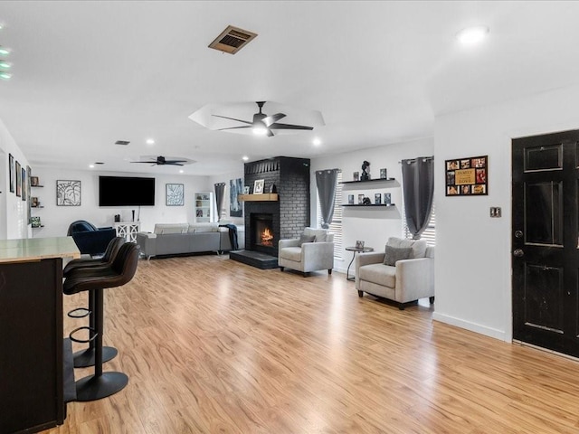 living room with light hardwood / wood-style floors, a brick fireplace, and ceiling fan