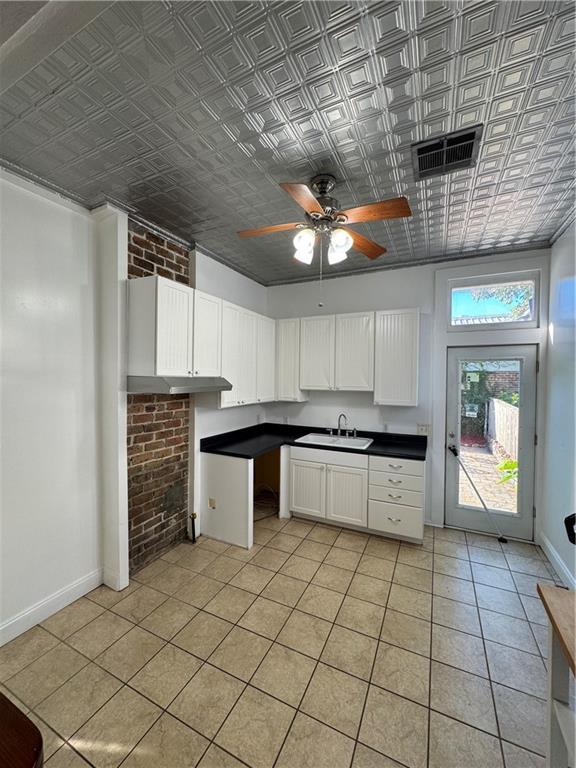 kitchen with crown molding, white cabinetry, sink, and brick wall