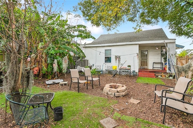 back of house featuring a yard, roof with shingles, fence, and a fire pit