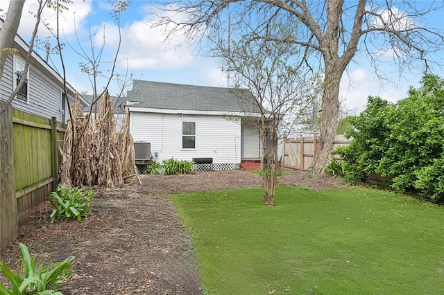 rear view of house featuring a yard, central air condition unit, fence private yard, and a shingled roof