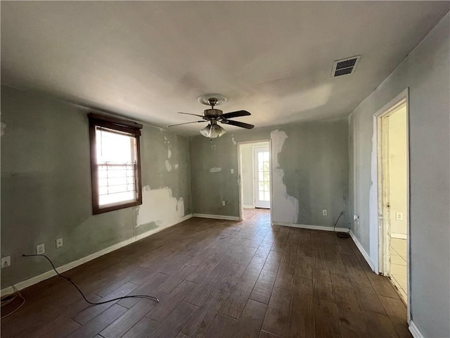 empty room featuring plenty of natural light, visible vents, ceiling fan, and dark wood-style flooring