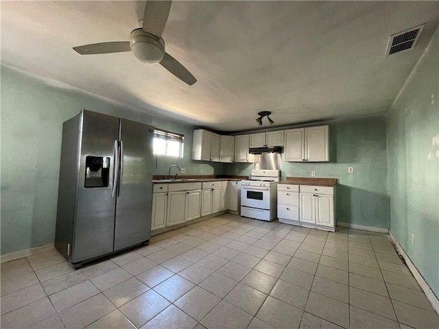 kitchen featuring light tile patterned floors, under cabinet range hood, visible vents, white gas range oven, and stainless steel fridge