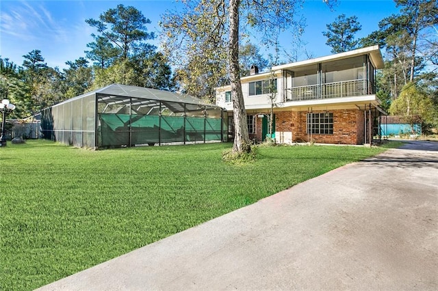 view of front facade featuring glass enclosure, a balcony, and a front lawn