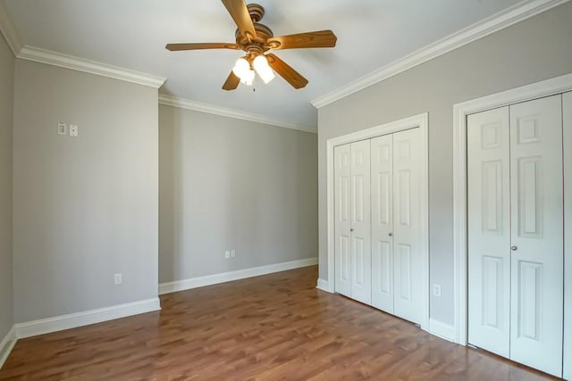 unfurnished bedroom featuring ceiling fan, wood-type flooring, crown molding, and multiple closets