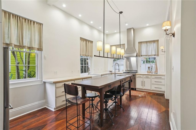 kitchen with decorative light fixtures, dark hardwood / wood-style flooring, and wall chimney range hood